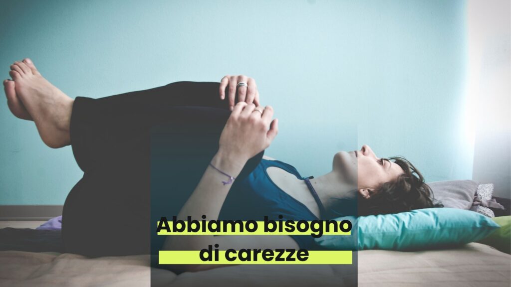 una persona (monja) stesa a terra si tiene le ginocchia tra le mani. Guarda verso l'alto. C'è una scritta: "Abbiamo bisogno di carezze"